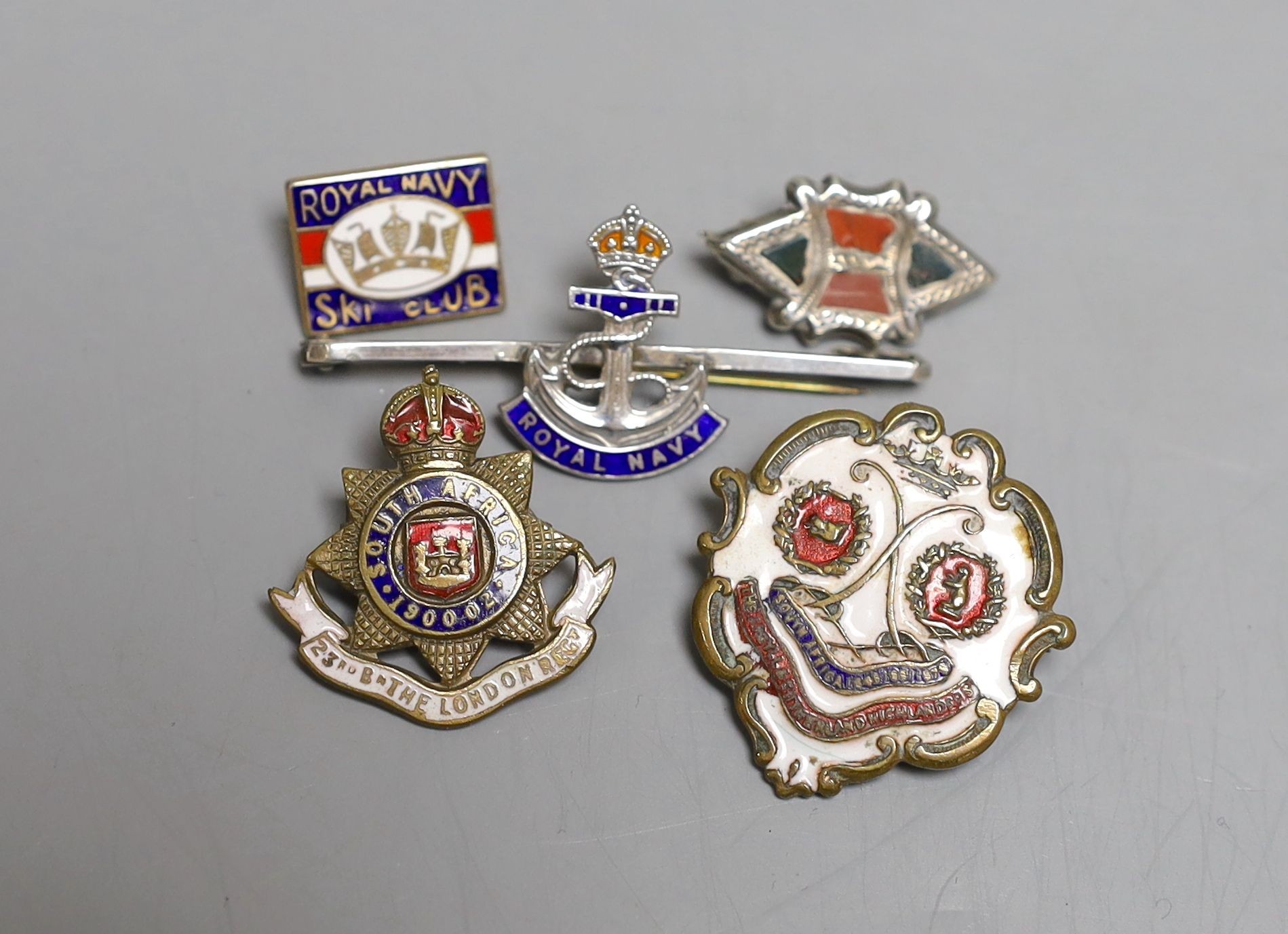 Four military badges: A Royal Navy badge and ski club badge, South Africa badge and another.